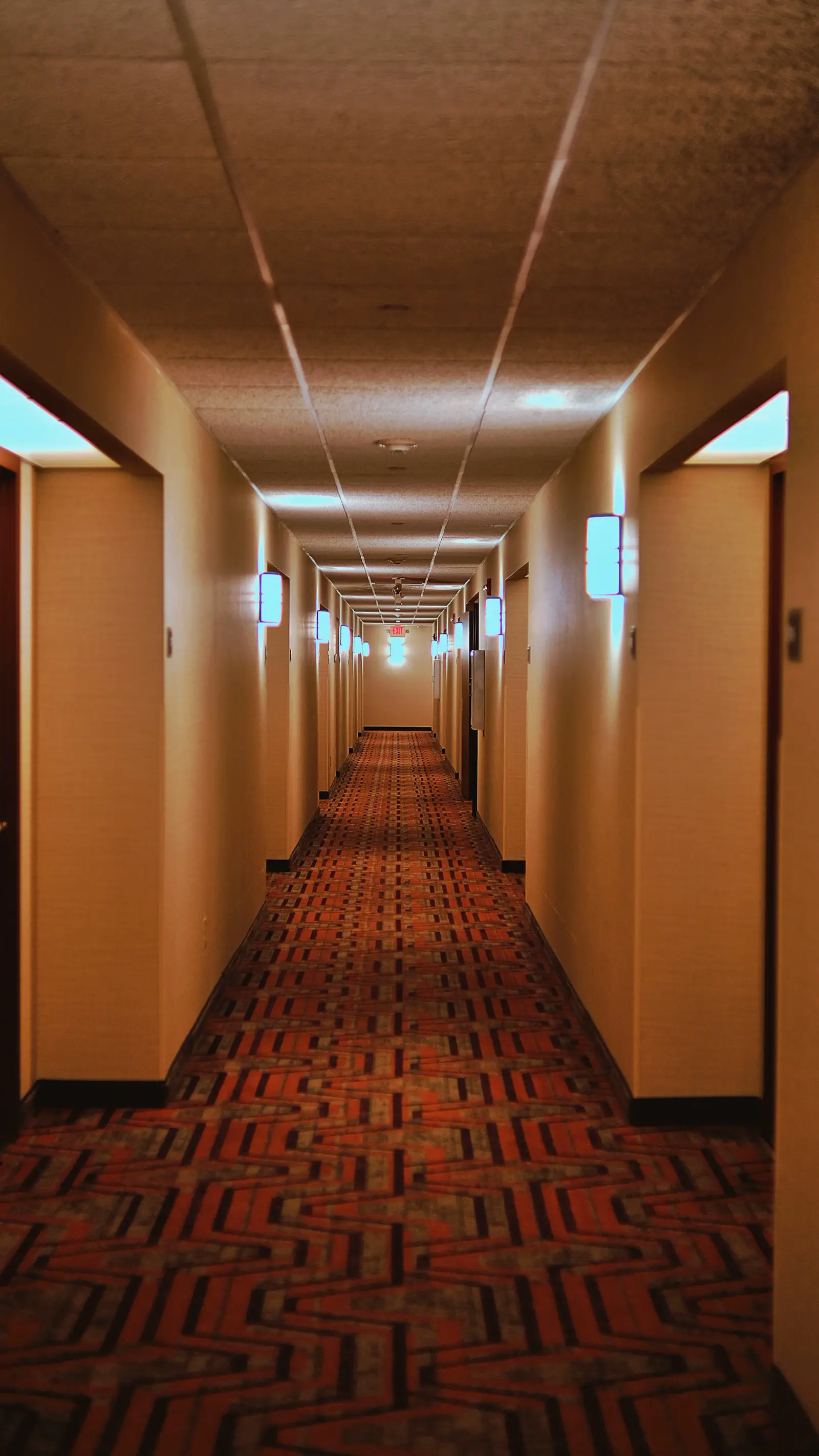 Long hotel corridor with patterned commercial carpet and guest-room doors